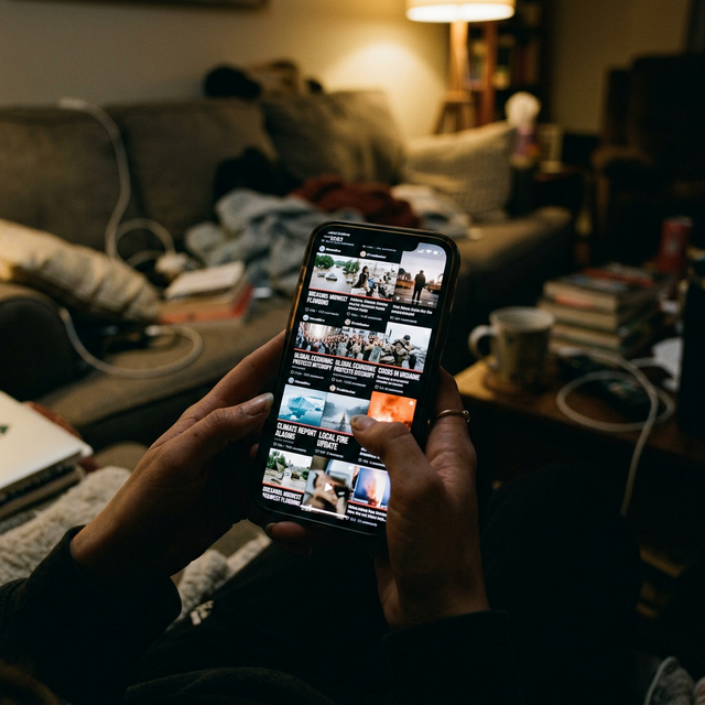 Person scrolling through phone on a couch in a dimly lit room